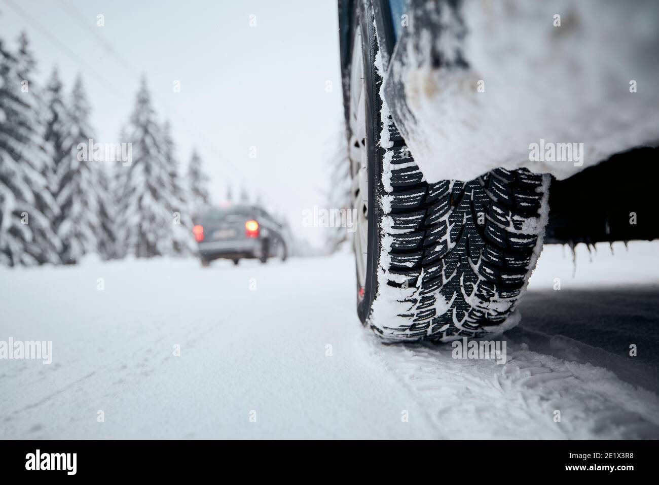 Nahaufnahme des Autoreifens auf schneebedeckter und vereister Straße. Themen Sicherheit und Fahren im Winter. Stockfoto