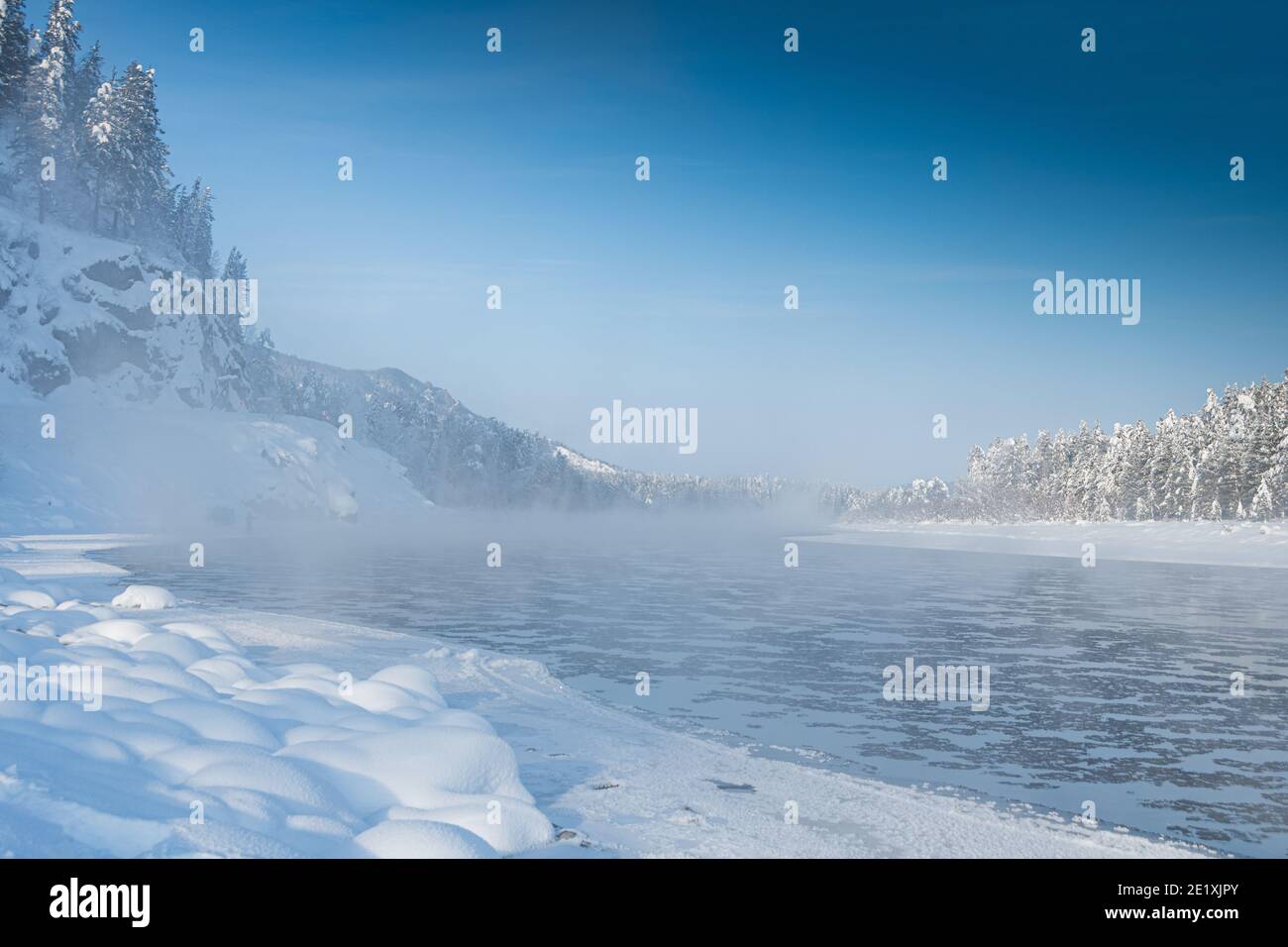 Frostiger Nebel über dem Winterfluss mit Schnee und Wald am Ufer. Erstes Eis am See an kalten Tagen. Stockfoto