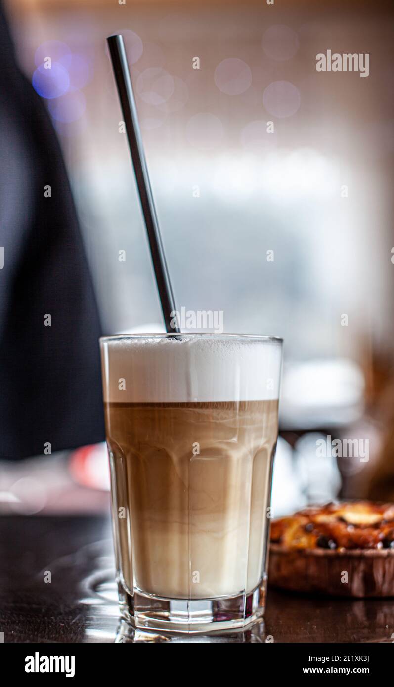 Heißer Latte-Kaffee in einem Glas und ein frischer Apfel-Dessert daneben. Das heiße Getränk wird mit einem Plastikstroh serviert. Leckeres Frühstück im Café Stockfoto