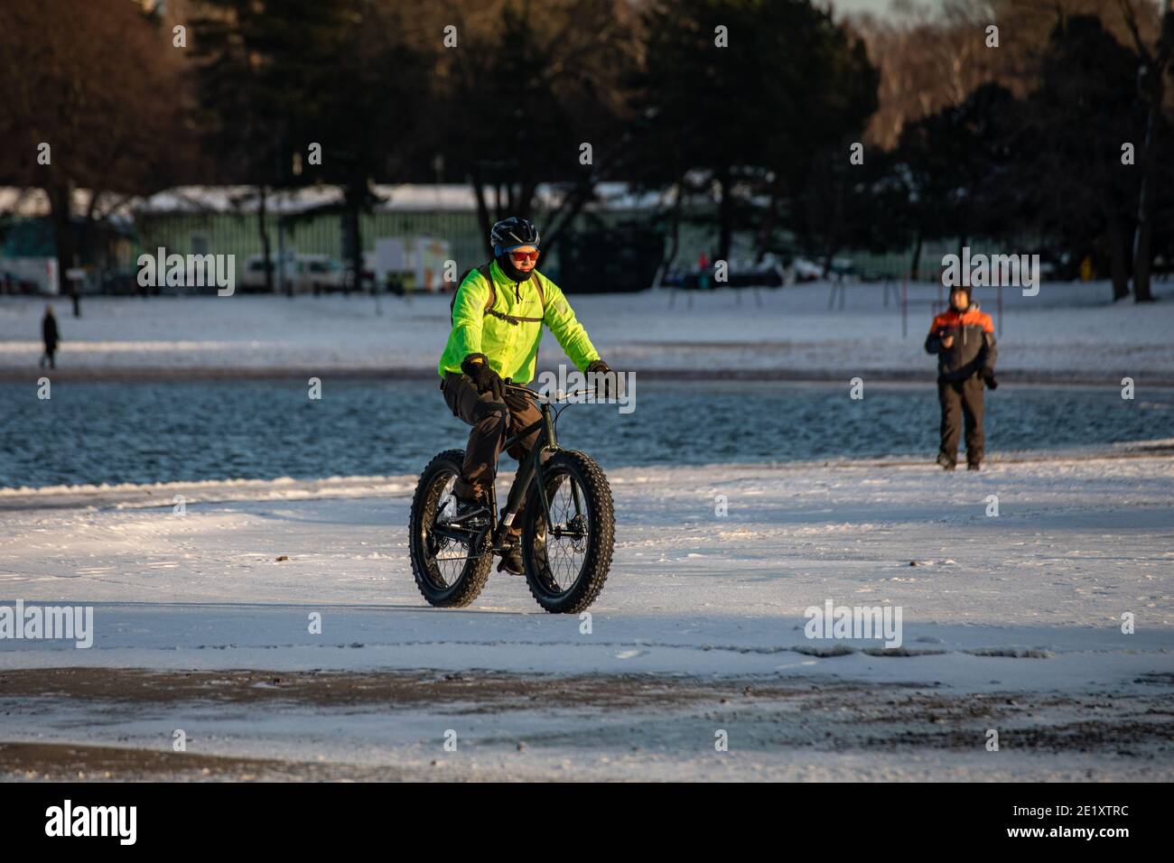 Radfahren im Winter. Mann trägt grüne Jacke Reiten Fett Fahrrad auf Hietaranta Strand im Winter. Helsinki, Finnland. Stockfoto