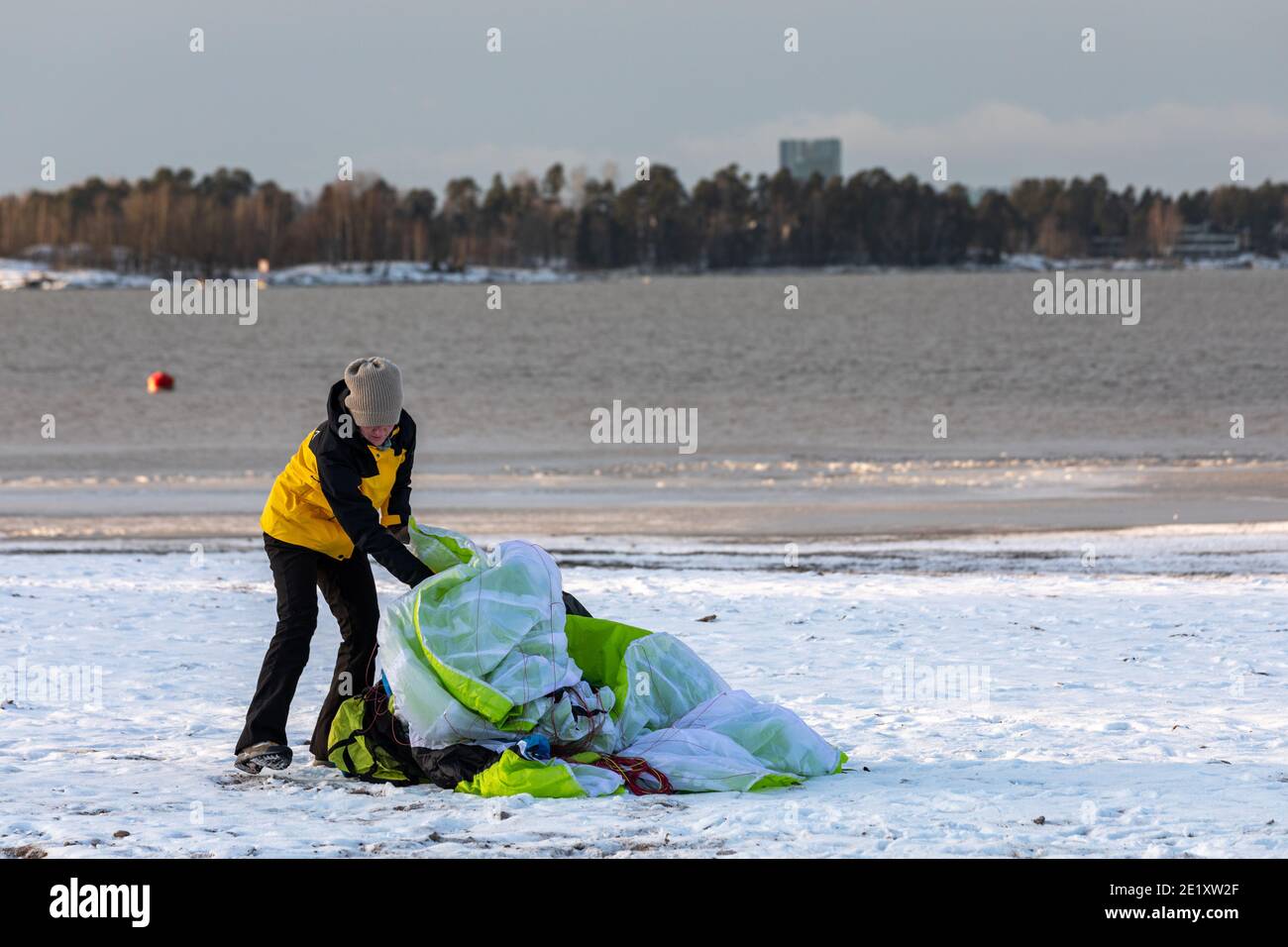 Frau beim Packen des Gleitschirms nach der Bodenbearbeitung am schneebedeckten Hietaranta Beach in Helsinki, Finnland Stockfoto