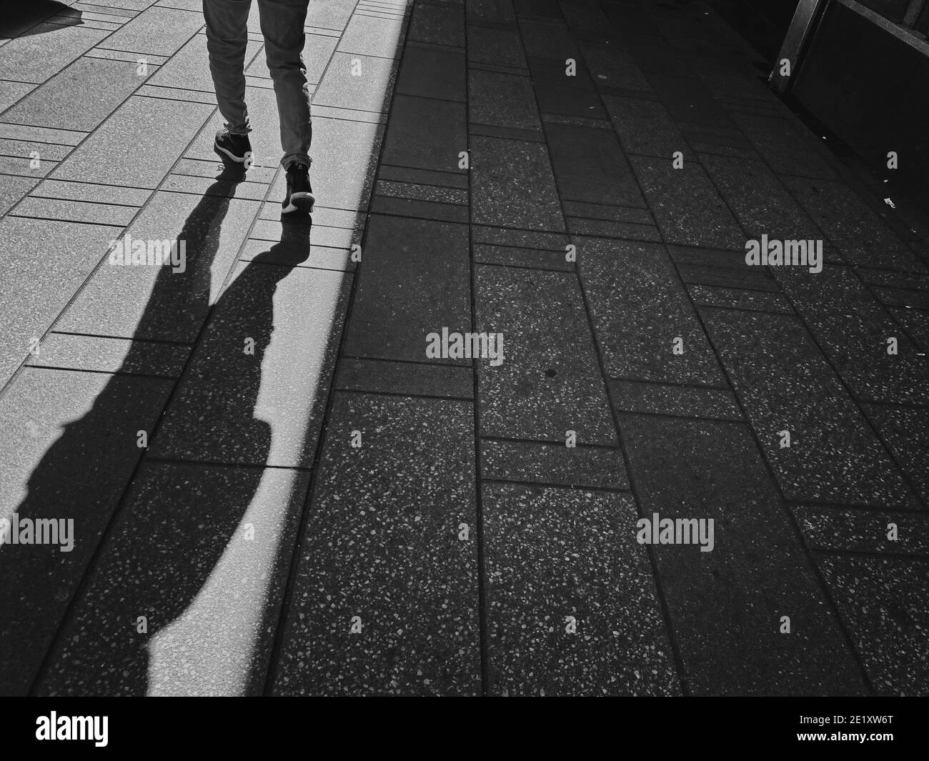 Mann mit Hosen und Turnschuhen, der lange Schatten auf dem Bürgersteig zeigt Stockfoto