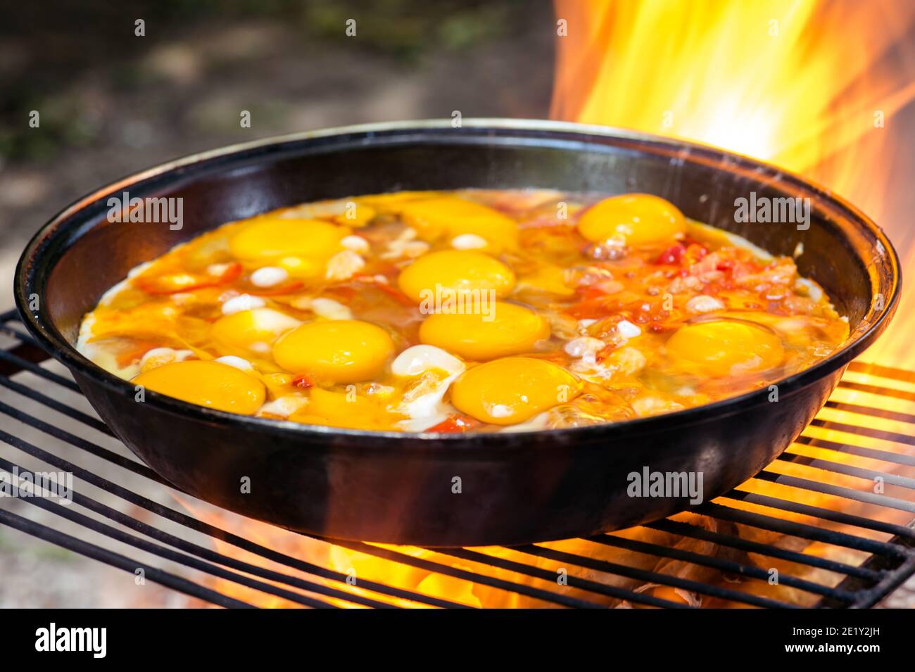 Spiegeleier mit Gemüse in einer Pfanne auf dem Grill close-up in der feurigen Flamme des Feuers. Das Konzept der Leichtigkeit des Kochens in der Natur. Selektiv f Stockfoto