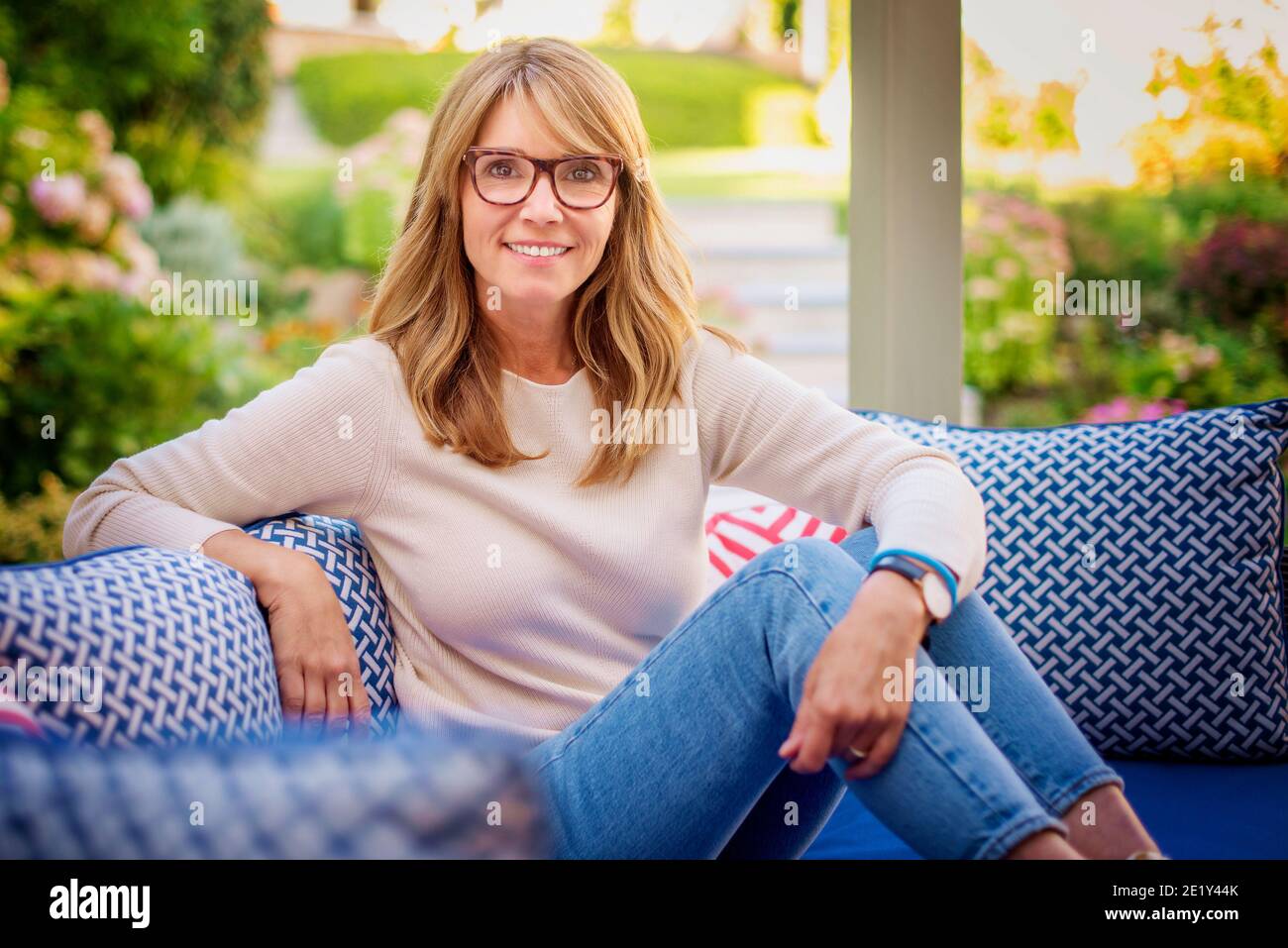 Porträt von mittleren Alters Attraktive Frau, die Kamera und lächelnd beim Entspannen auf dem Balkon zu Hause. Stockfoto