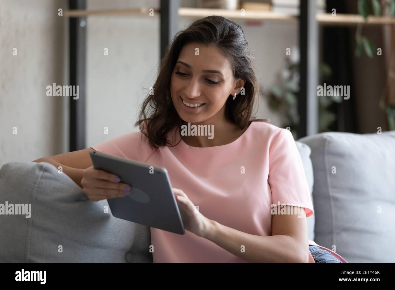 Lächelnde ethnische Frau Entspannen Sie sich zu Hause mit Tablet Stockfoto