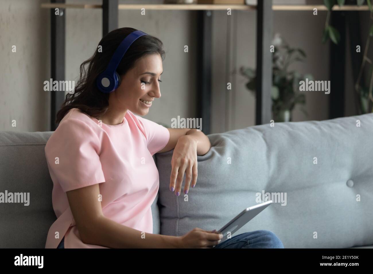 Glückliche ethnische Frau in Kopfhörer sprechen auf Tablet Stockfoto