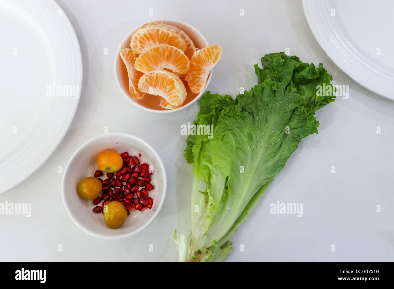 Frisch geschälte Orangen mit Granatapfel und Sellerie-Blättern angeordnet Ein Tisch mit teilweise weißen Platten in den Ecken Stockfoto
