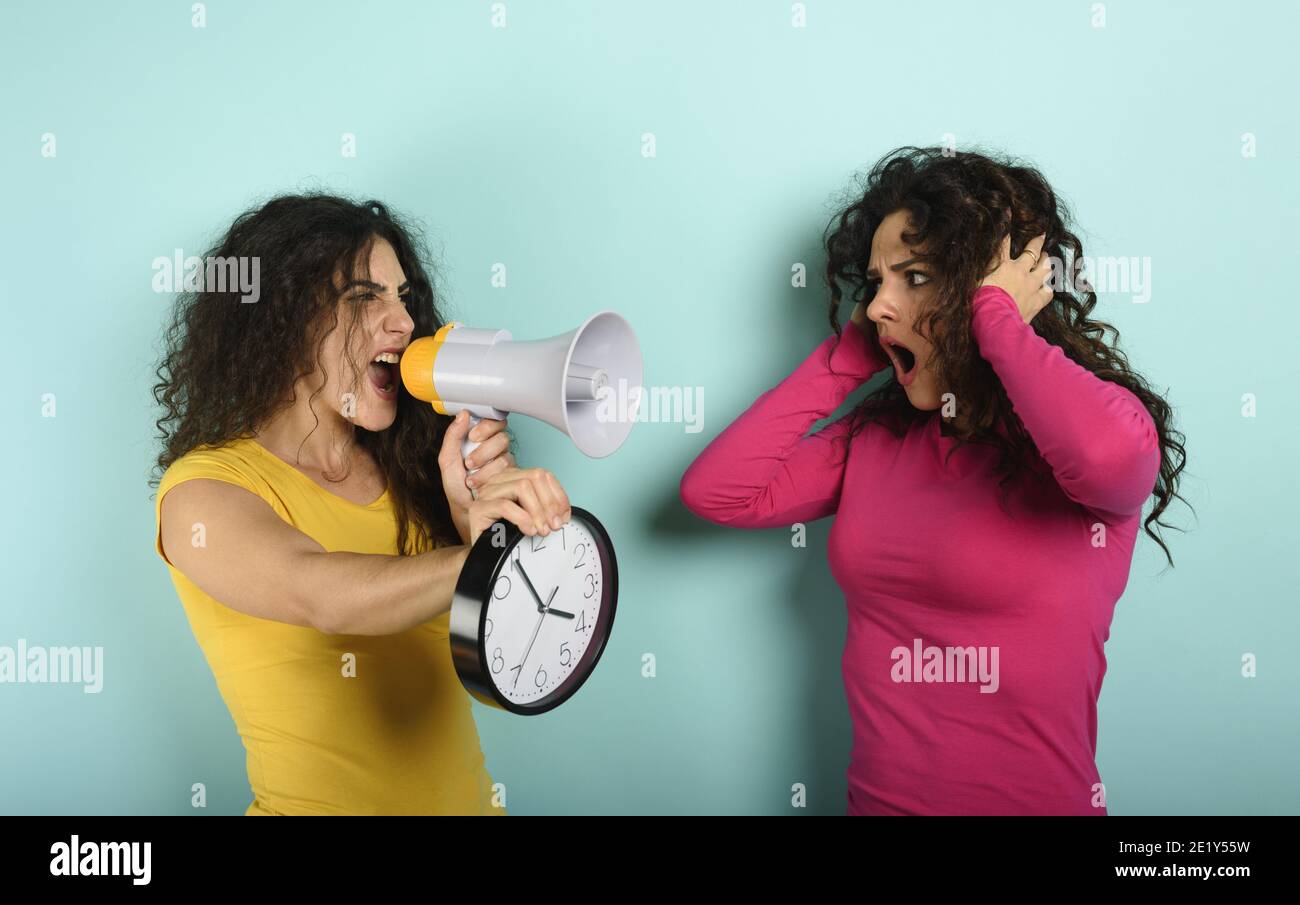 Frau schreit mit Lautsprecher zu einem Freund, weil es zu spät ist. Wütend Ausdruck. Cyan Hintergrund Stockfoto