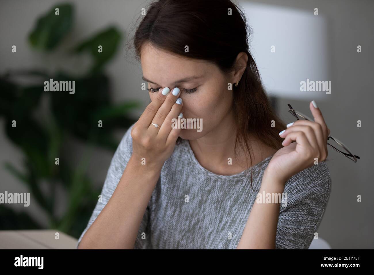 Müde junge Frau massiert die Augen mit Kopfschmerzen Stockfoto