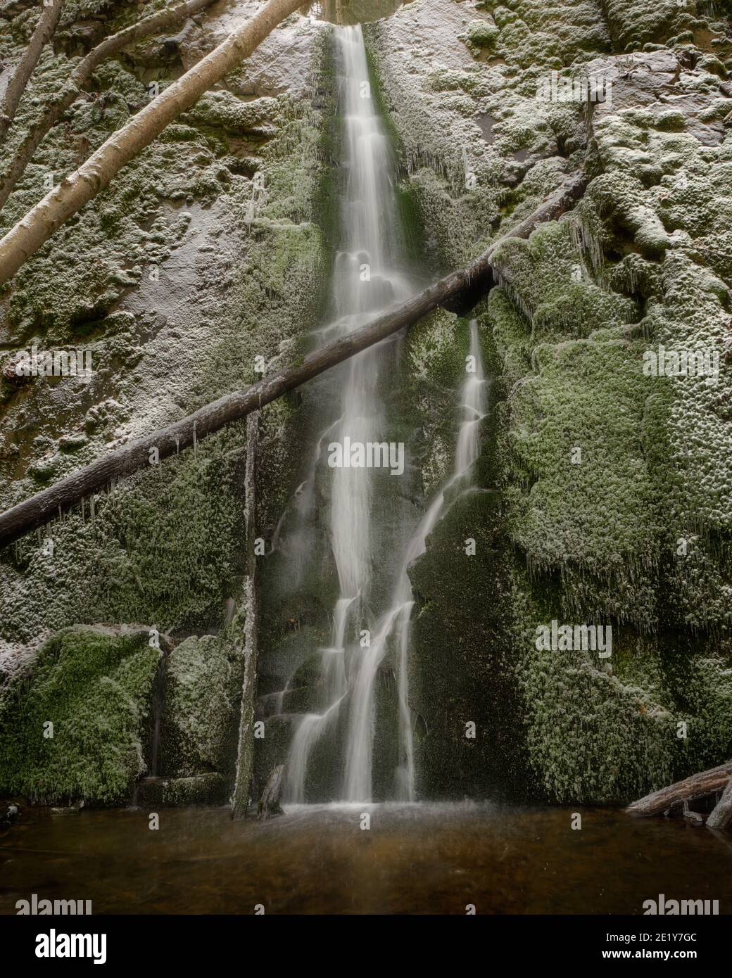Baumstämme liegen über einem Wasserfall mit Moos und Schnee An den Seiten Stockfoto