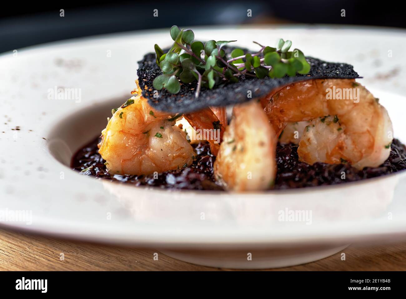 Risotto mit schwarzem Reis. Garnelen Risotto auf einem weißen Teller auf dem Tisch, serviert in einem Restaurant, Menü Food-Konzept. Stockfoto