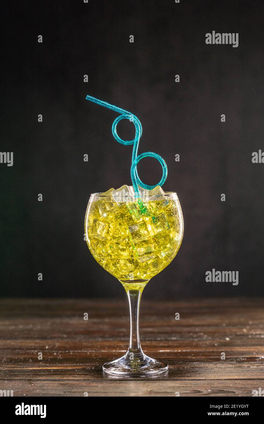 Gelber Cocktail in einem mit Eis gefüllten Glas, das mit Erdbeeren dekoriert ist Mit blauen Locken Party flexible Kunststoff Stroh Stockfoto