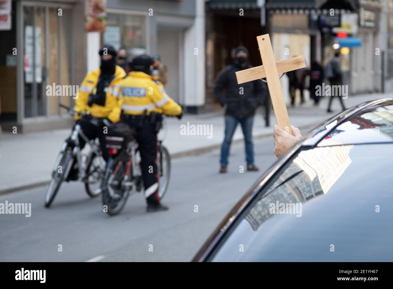 Als Reaktion auf die Geldstrafe von Kirchenbesuchern hält ein Kaplan bei einem Protest gegen die COVID-19-Sperre in Toronto, Ontario, ein Kreuz vor der Polizei. Stockfoto