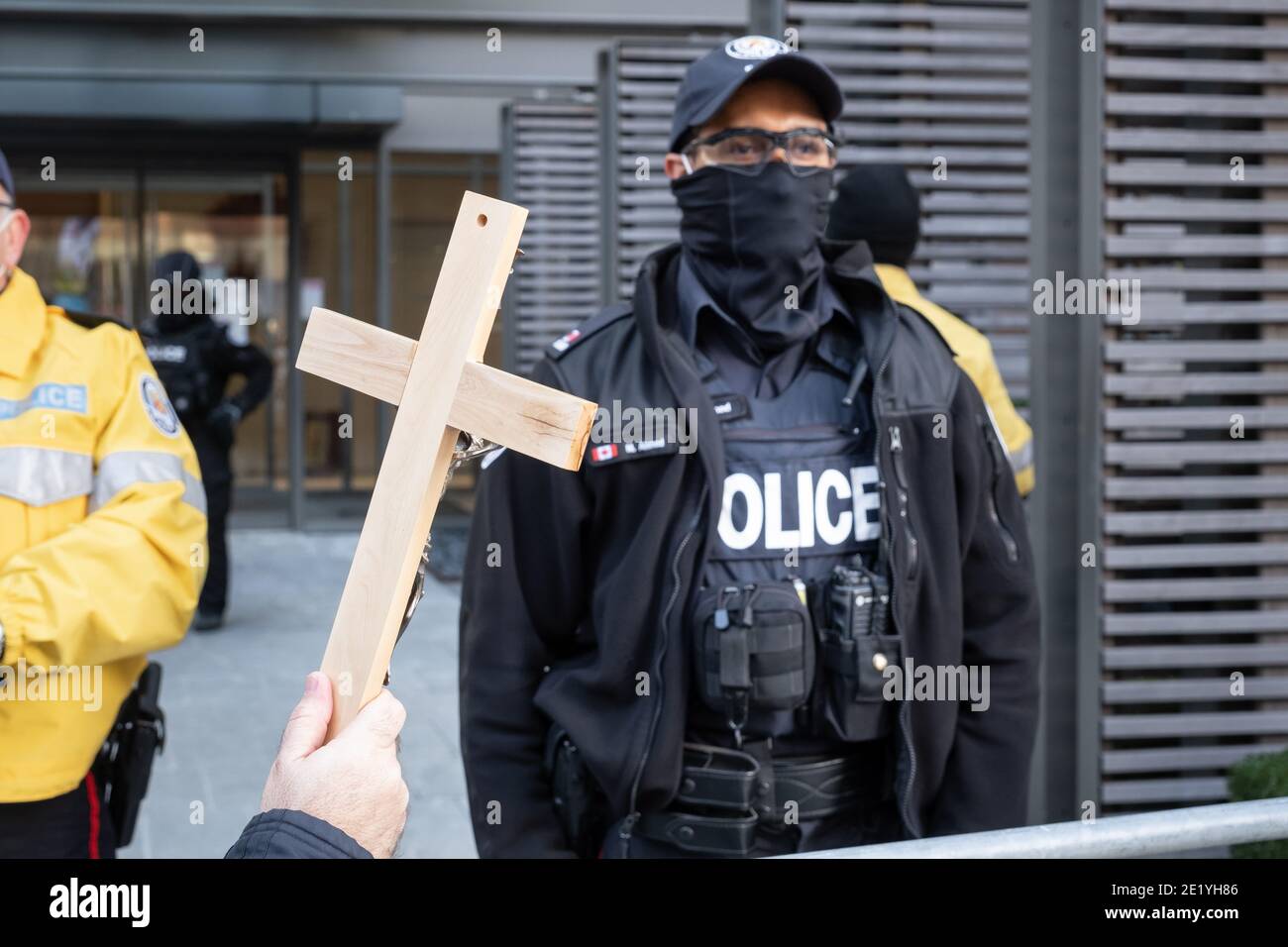 Als Reaktion auf die Geldstrafe von Kirchenbesuchern hält ein Kaplan bei einem Protest gegen die COVID-19-Sperre in Toronto, Ontario, ein Kreuz vor der Polizei. Stockfoto