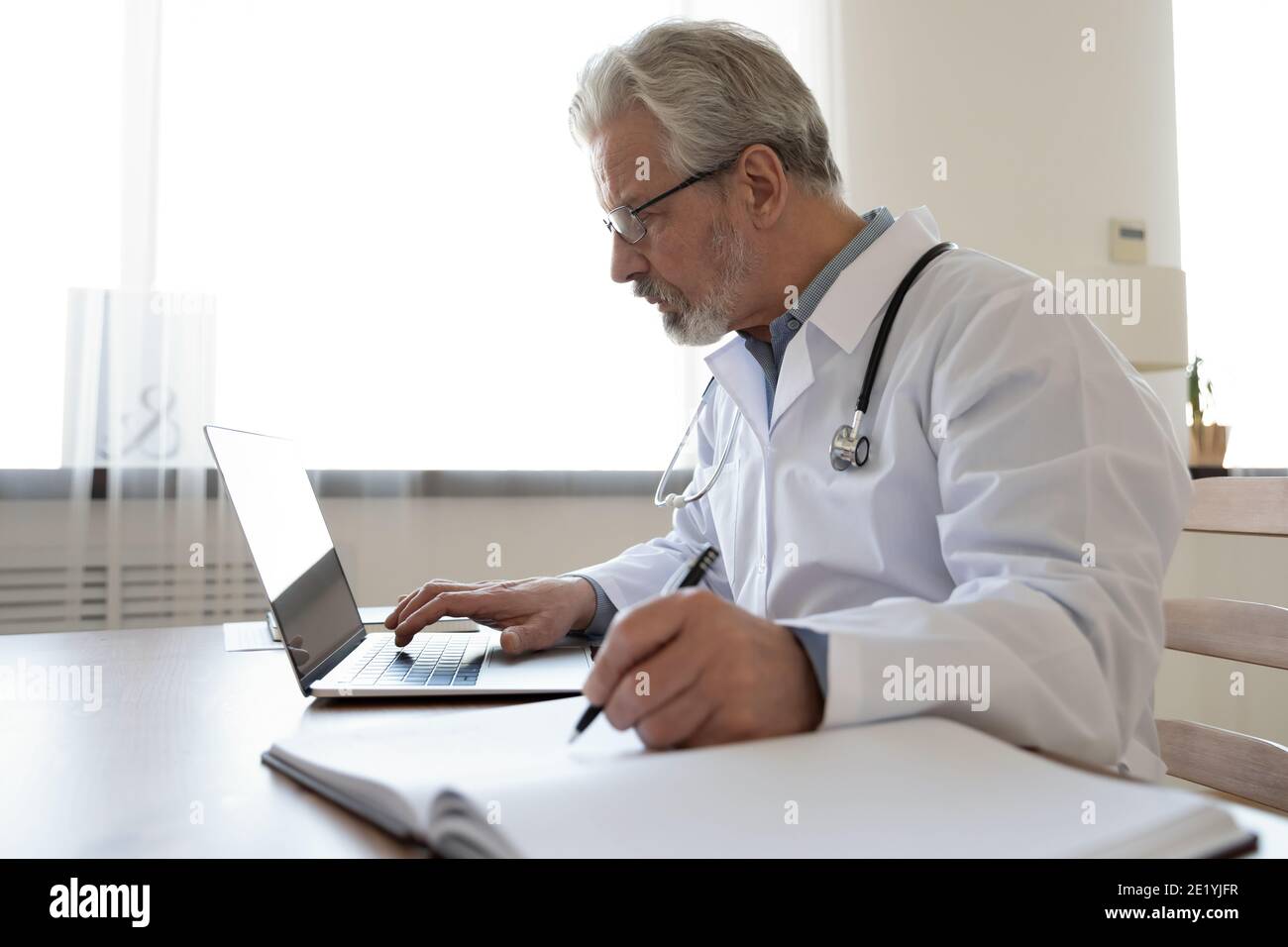 Konzentrierte 60er Jahre reifer Arzt allein in der Klinik Büro arbeiten. Stockfoto
