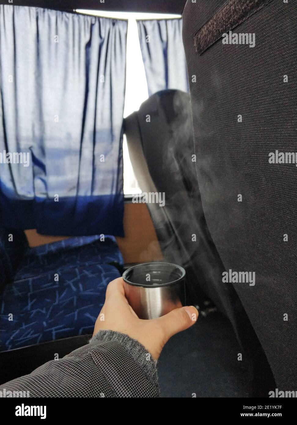 Ein Mann hält in der Hand eine Kappe aus einer Thermoskanne mit dampfendem heißen Tee, in der Kabine des Busses. Heißes Getränk während der Reise. Stockfoto