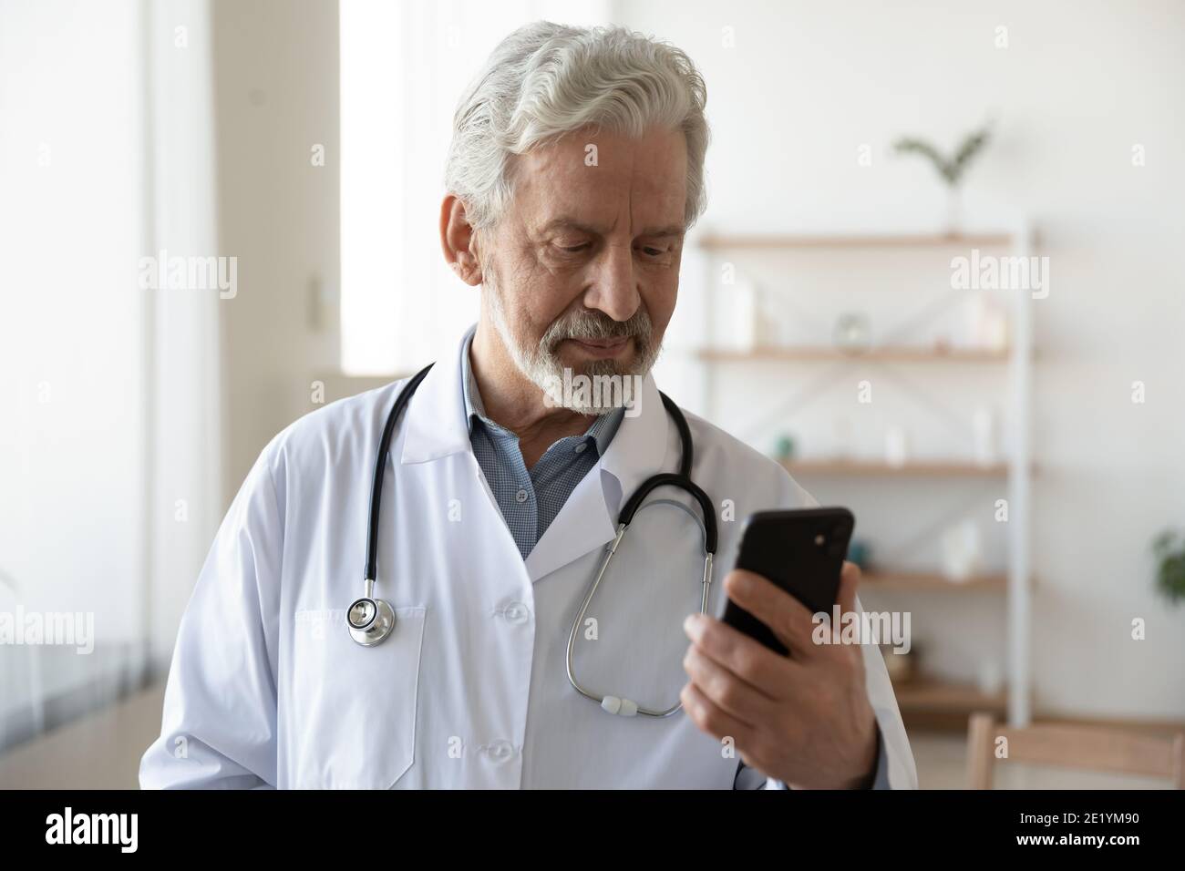 Älterer Arzt im mittleren Alter mit Smartphone-Apps. Stockfoto