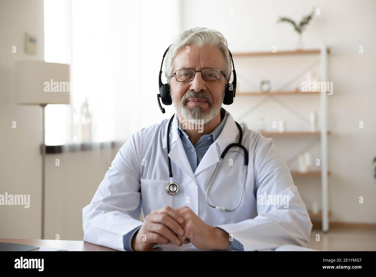 Glücklicher Arzt mittleren Alters im Headset mit Videoanruf. Stockfoto