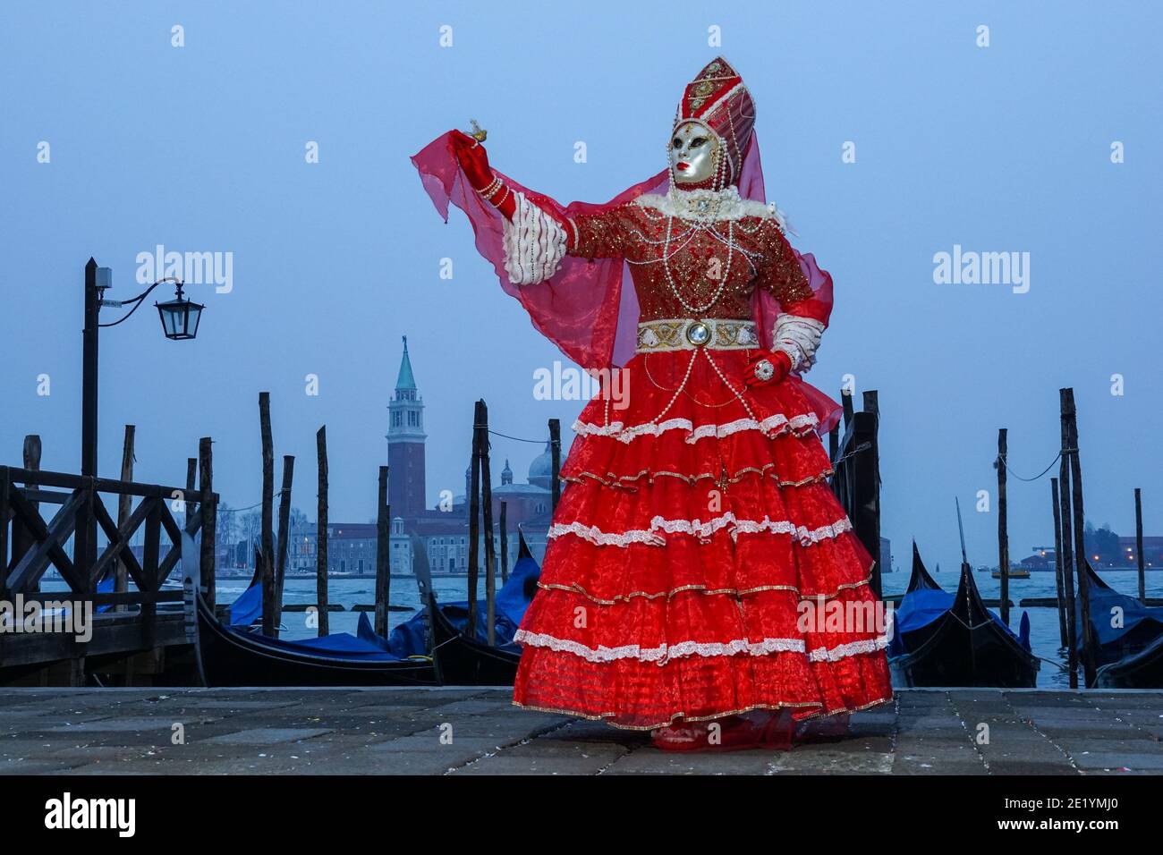 Frau in traditionell dekoriertem Kostüm und Maske während des Karnevals in Venedig gekleidet mit dem Kloster San Giorgio im Hintergrund Venedig, Italien Stockfoto