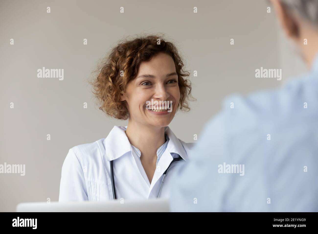 Glückliche junge hübsche weibliche Hausärztin, die dem Patienten zuhört. Stockfoto