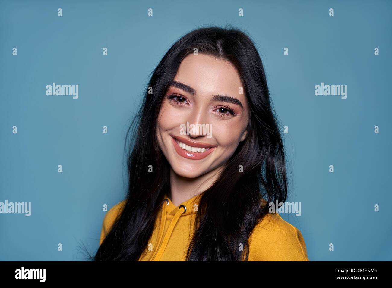 Lächelnd asiatisch gen z teen Mädchen Blick auf Kamera auf blauem Hintergrund. Hochformat Stockfoto