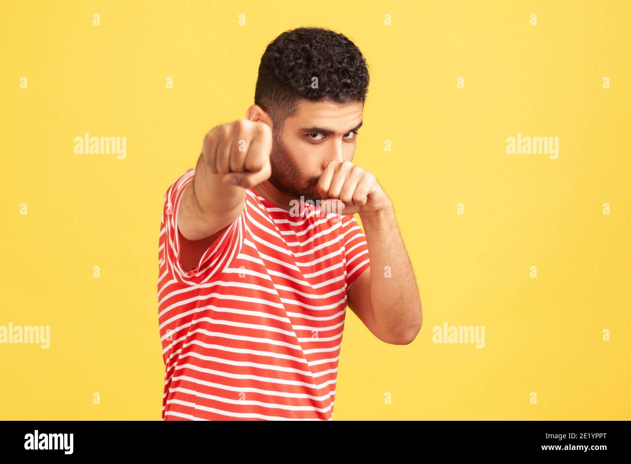Ich werde Euch schlagen! Aggressiver bärtiger Mann im gestreiften T-Shirt stehend mit erhobenen Fäusten Boxgeste, bereit zu schlagen, bereit zu kämpfen, Kampfgeist. Stockfoto