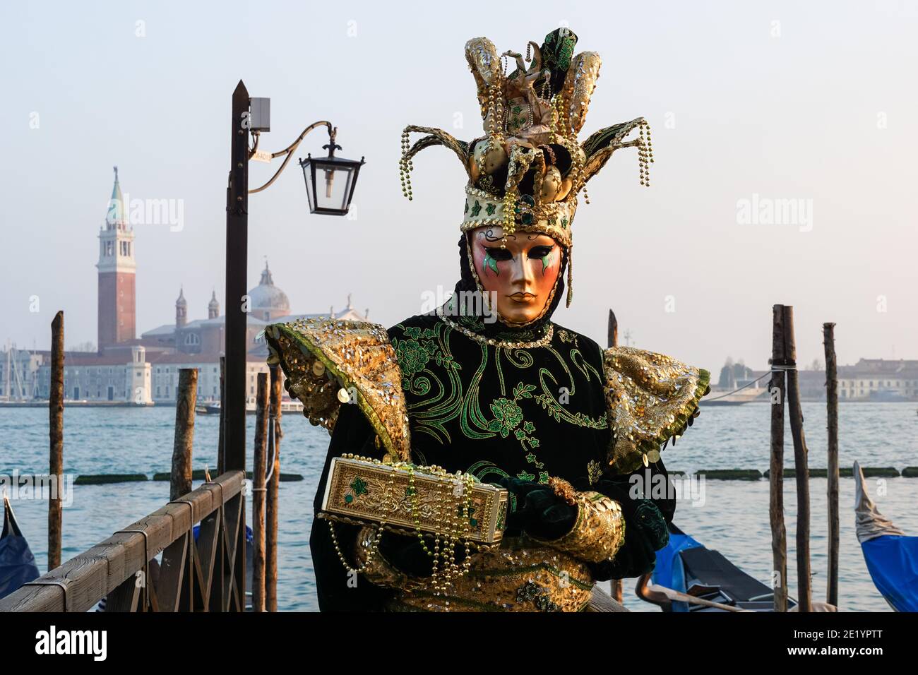 Mann in traditionell dekoriertem Kostüm und bemalte Maske während des Karnevals von Venedig mit dem Kloster San Giorgio dahinter, Venedig, Italien Stockfoto