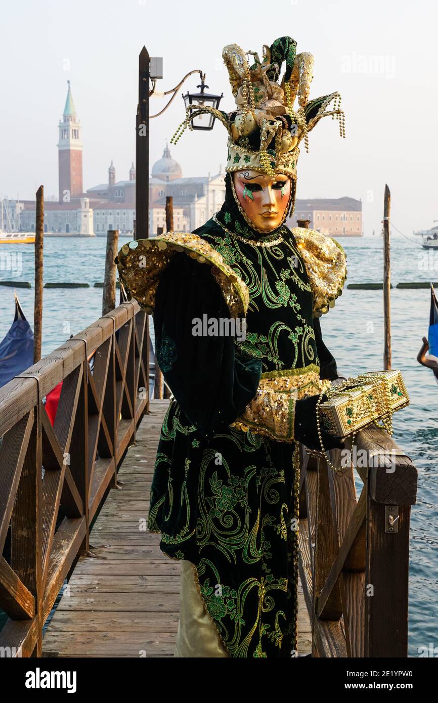 Mann in traditionell dekoriertem Kostüm und bemalte Maske während des Karnevals von Venedig mit dem Kloster San Giorgio dahinter, Venedig, Italien Stockfoto