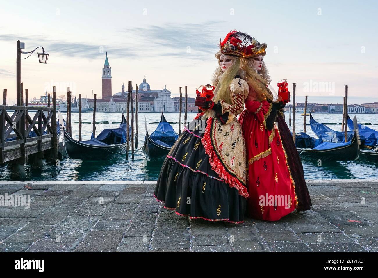 Zwei Frauen in traditionell dekorierten Kostümen und bemalten Masken während des Karnevals in Venedig mit dem Kloster San Giorgio hinter Venedig, Italien Stockfoto