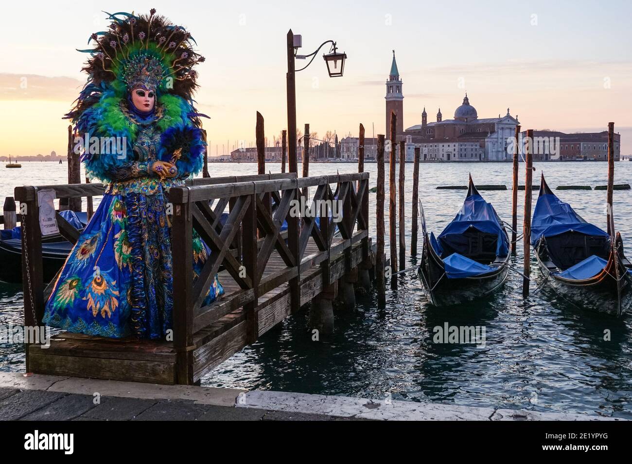Frau in traditionell dekoriertem Kostüm und bemalter Maske während des Karnevals in Venedig mit dem Kloster San Giorgio dahinter, Venedig, Italien Stockfoto
