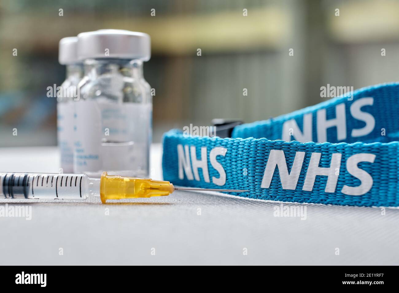 Stafford, Vereinigtes Königreich - Januar 10 2021: NHS-Impfstoff-Konzept. Spritze, Injektionsfläschchen und NHS-Trageschlaufe. Selektiver Fokus. Stockfoto