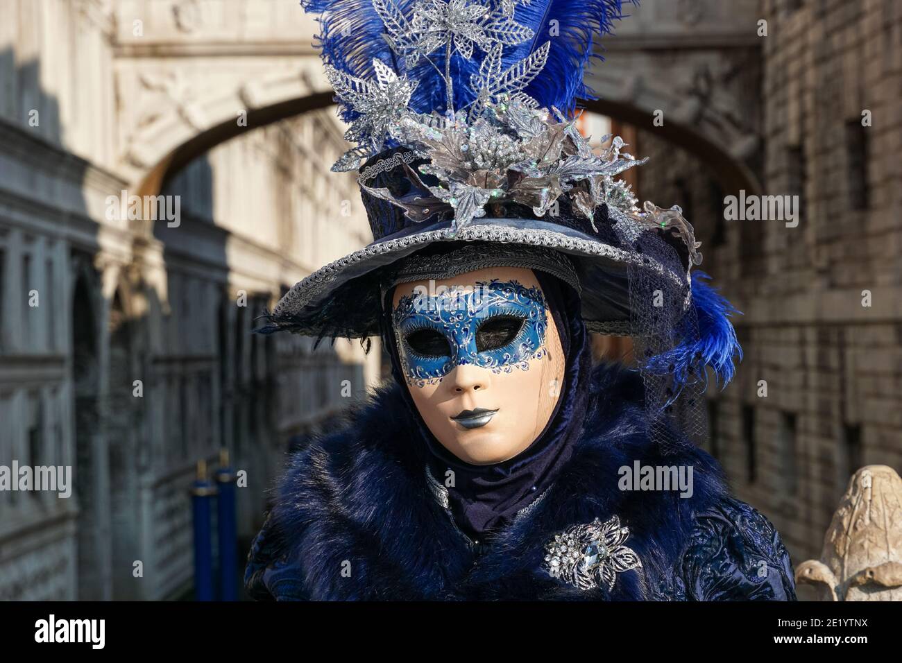 Frau in traditionell dekoriertem Kostüm mit Hut und bemalter Maske während des Karnevals in Venedig mit der Seufzerbrücke dahinter, Venedig Italien Stockfoto