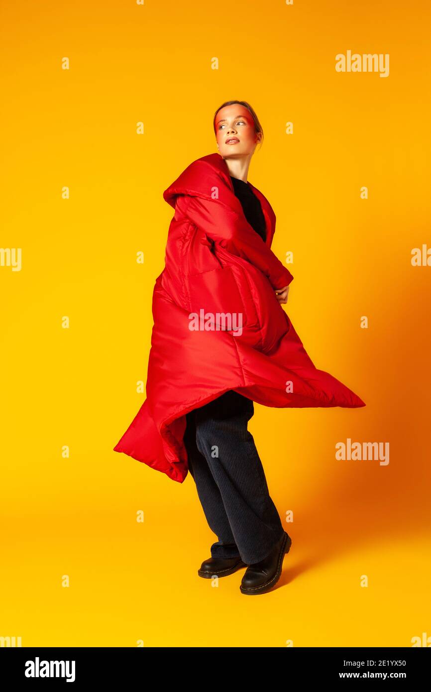 Weibliches Modell im baggy Mantel, der sich vor gelbem Hintergrund dreht Stockfoto