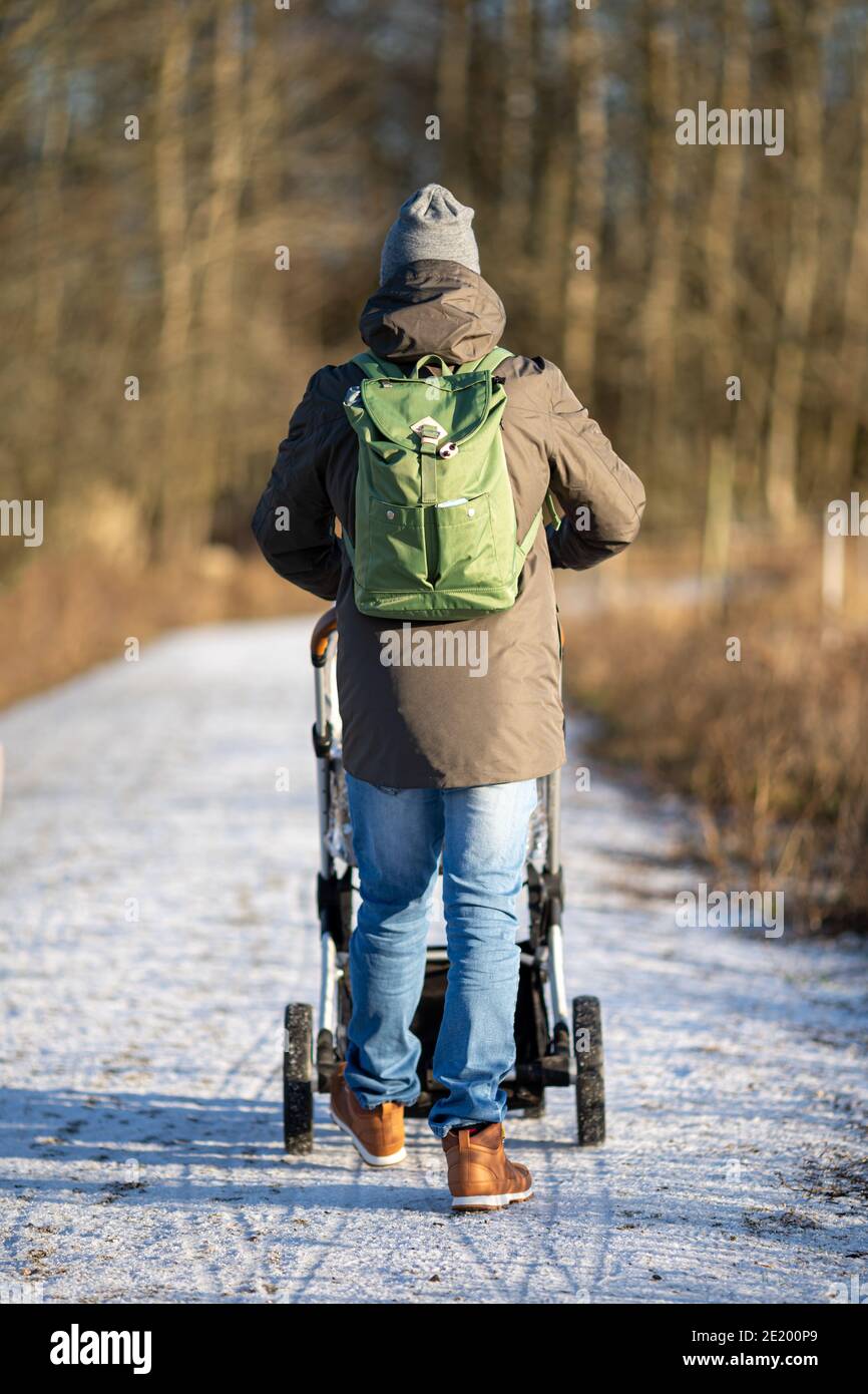 Junge moderne Papa mit Rucksack zu Fuß mit Kinderwagen in der Wald Stockfoto