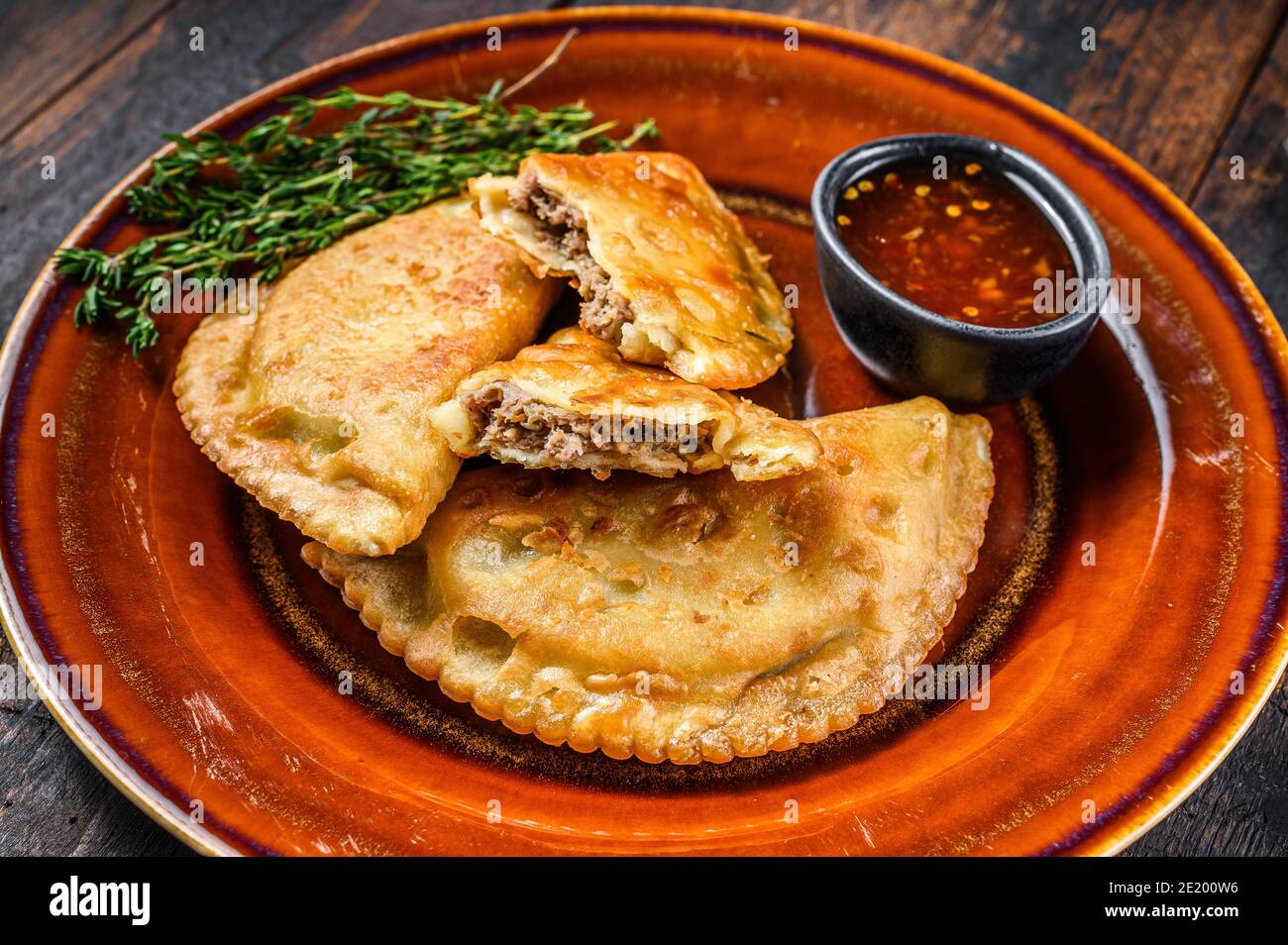 Gebratene Empanadas mit Hackfleisch auf einem Teller mit Chilisauce serviert. Dunkler Holzhintergrund. Draufsicht Stockfoto