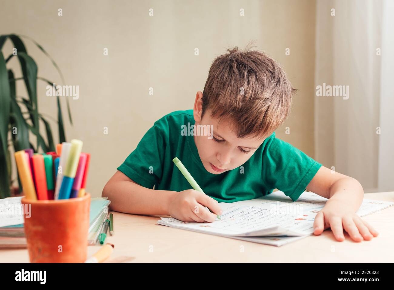 Nettes 7 Jahre altes Kind, das seine Hausaufgaben macht, am Schreibtisch sitzend. Junge schreiben in Notebook. Stockfoto