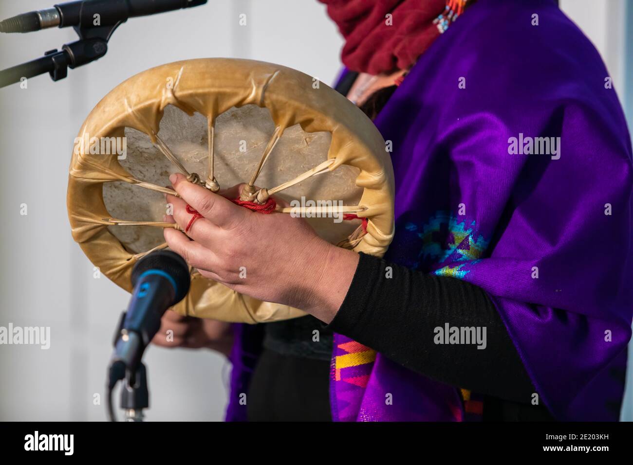Sound-Demonstration während eines nativen Trommelworkshops. Frau in farbigen nativen Schal Holing eine Sand gemacht Trommel vor einem Mikrofon, bereit, durchzuführen. Stockfoto