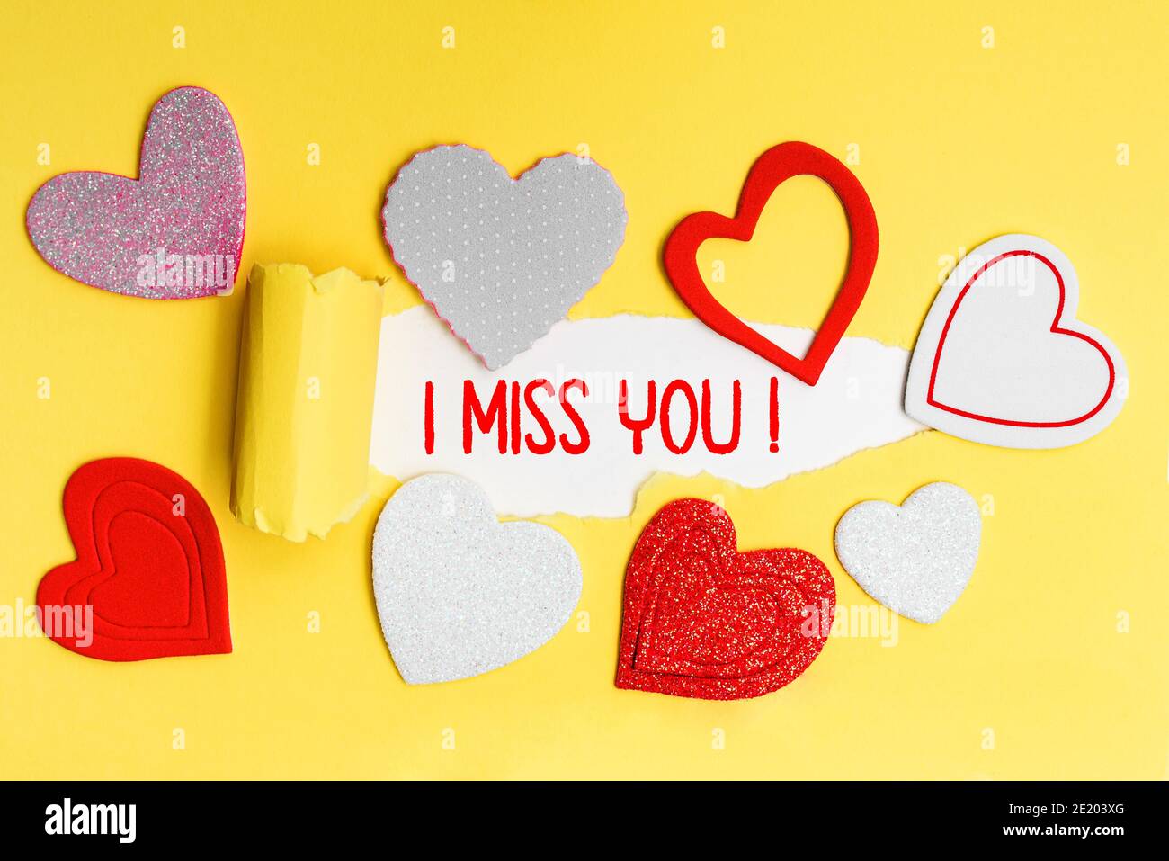 Deutscher Text I Miss You in roten Buchstaben auf einer gelben Karte mit Liebesherzen geschrieben. Stockfoto