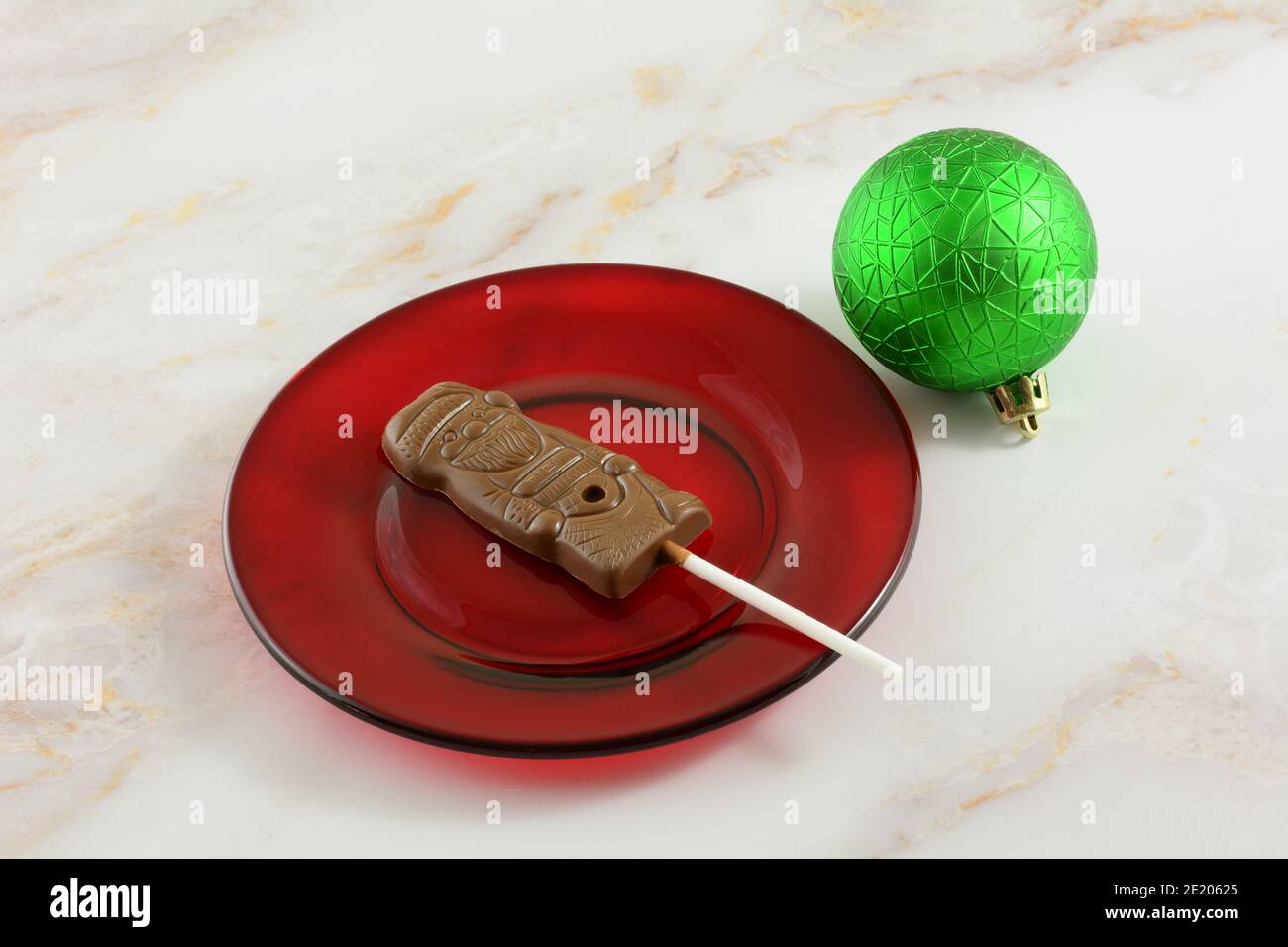 Vollmilchschokolade Weihnachtsmann auf einem Stock auf rotem Dessert Teller mit grünen Weihnachtsschmuck Stockfoto