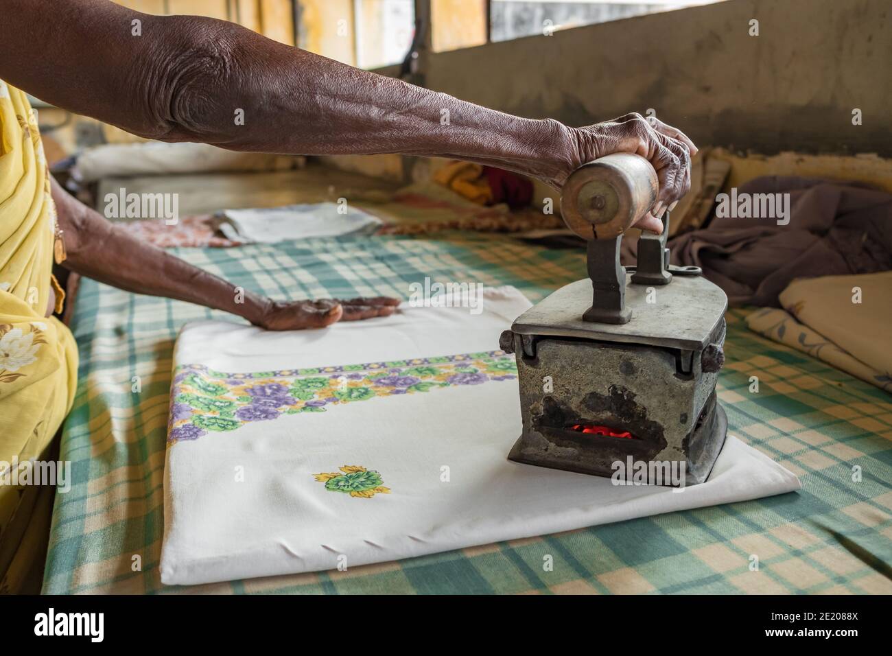 Undidentified ältere Frau Bügeln Kleidung mit einer alten Kohle beheizt Eisen in Indien Stockfoto