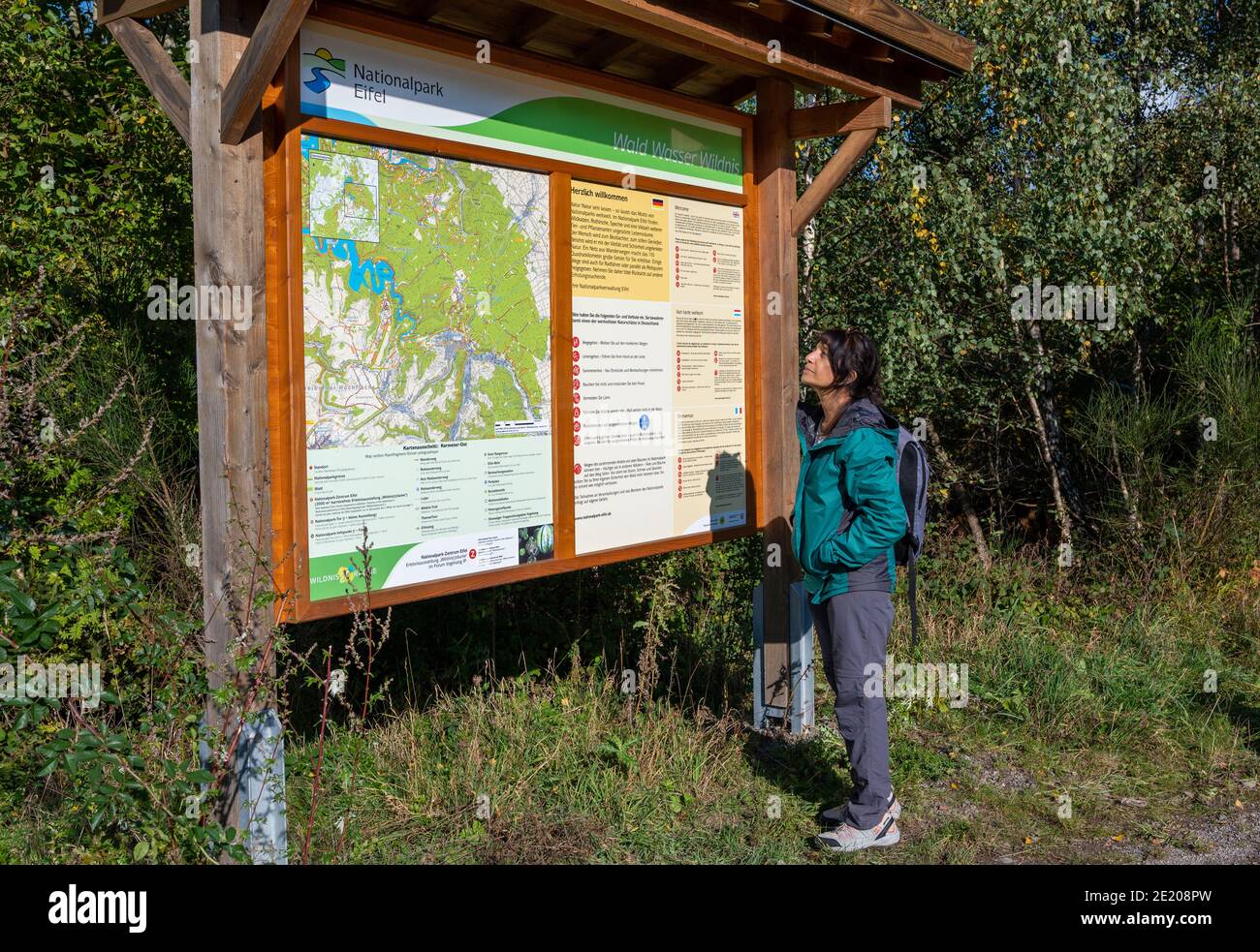 Asiatin beim Wandern im Nationalpark Eifel in Südwestdeutschland liest mehrsprachiges Informationsschild. Stockfoto