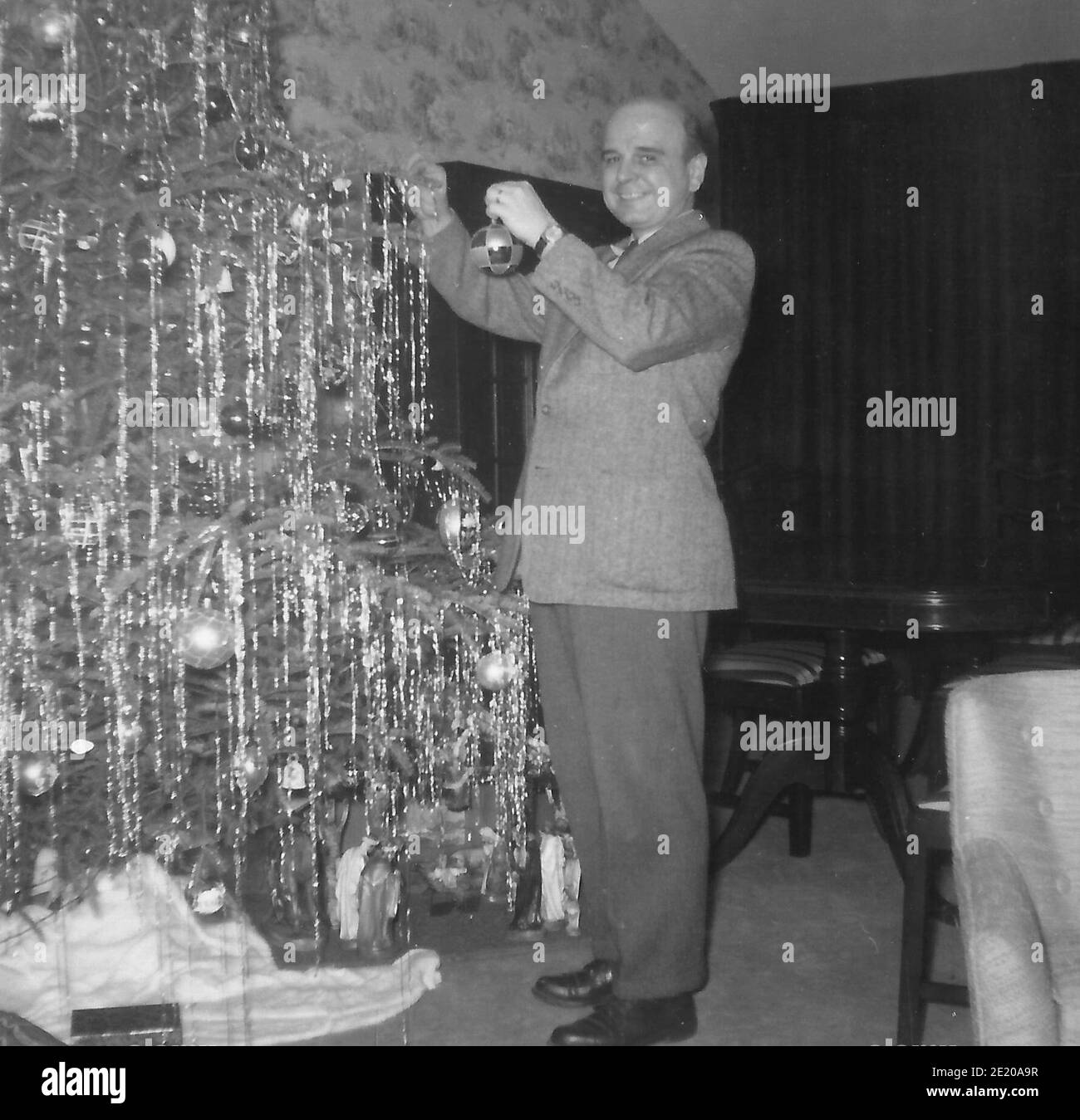 Ein Mann in einem Anzug, der einen Weihnachtsbaum schmückt - 1958 Stockfoto