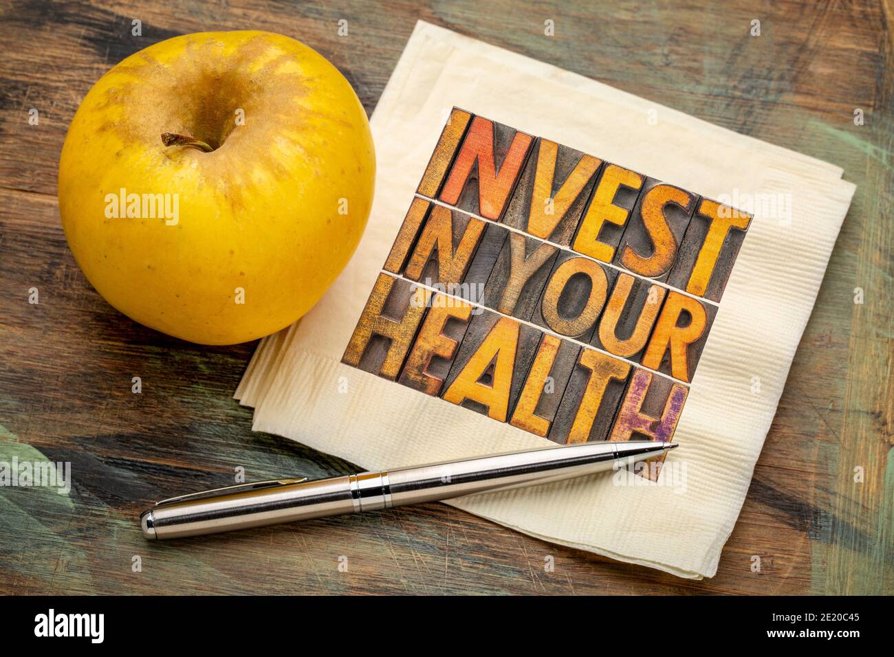Investieren Sie in Ihr Gesundheitskonzept - Wortabstrakt im Vintage-Buchdruck Holzart auf einer Serviette mit Apfel, gesunder Lebensstilberatung Stockfoto