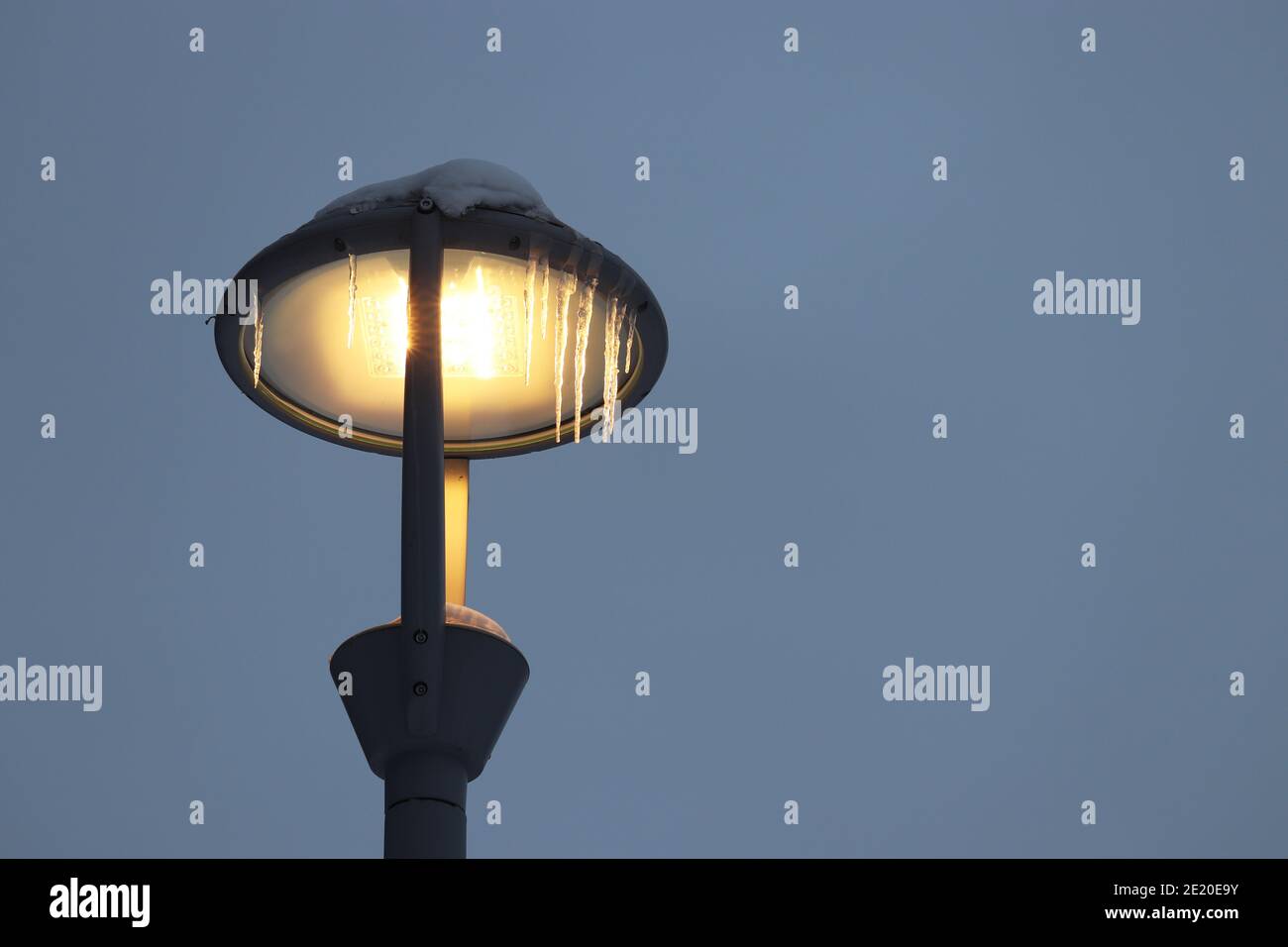 Glühende LED-Lampe mit Eiszapfen auf Winter Himmel Hintergrund bedeckt. Elektrische Beleuchtung, energiesparende Straßenlaterne Stockfoto