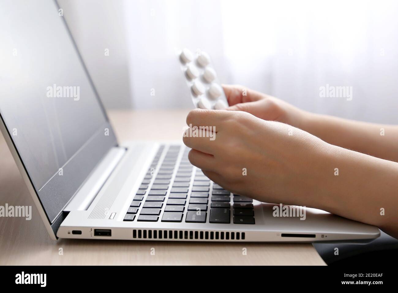 Weibliche Hände mit Pillen auf Laptop-Tastatur. Frau, die während der Arbeit Medikamente nimmt, die Kontraindikationen im Internet liest Stockfoto
