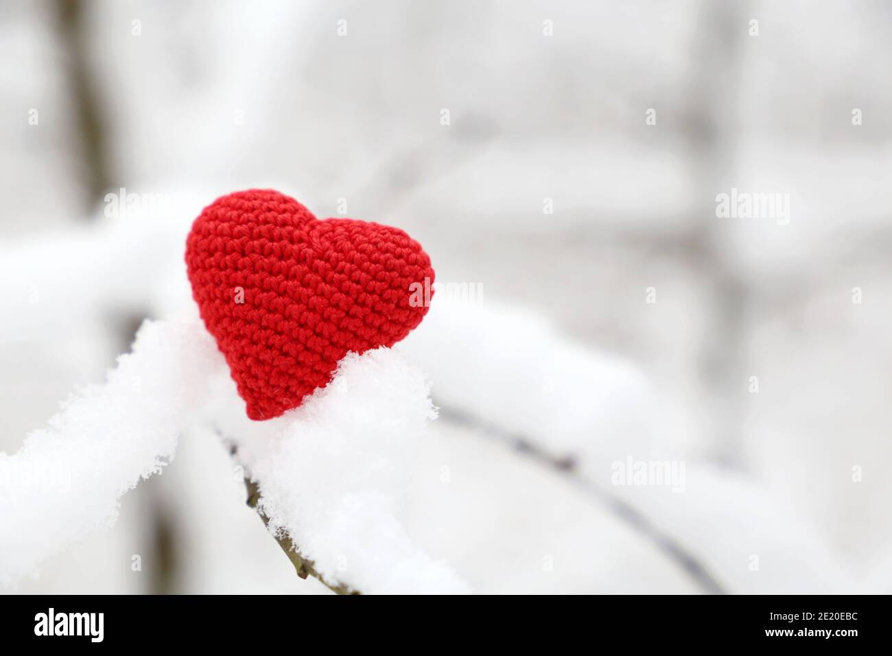 Valentine Herz im Winterwald, kaltes Wetter. Rot gestricktes Herz auf verschneiten Ast, Symbol der romantischen Liebe, Hintergrund für Urlaub Stockfoto