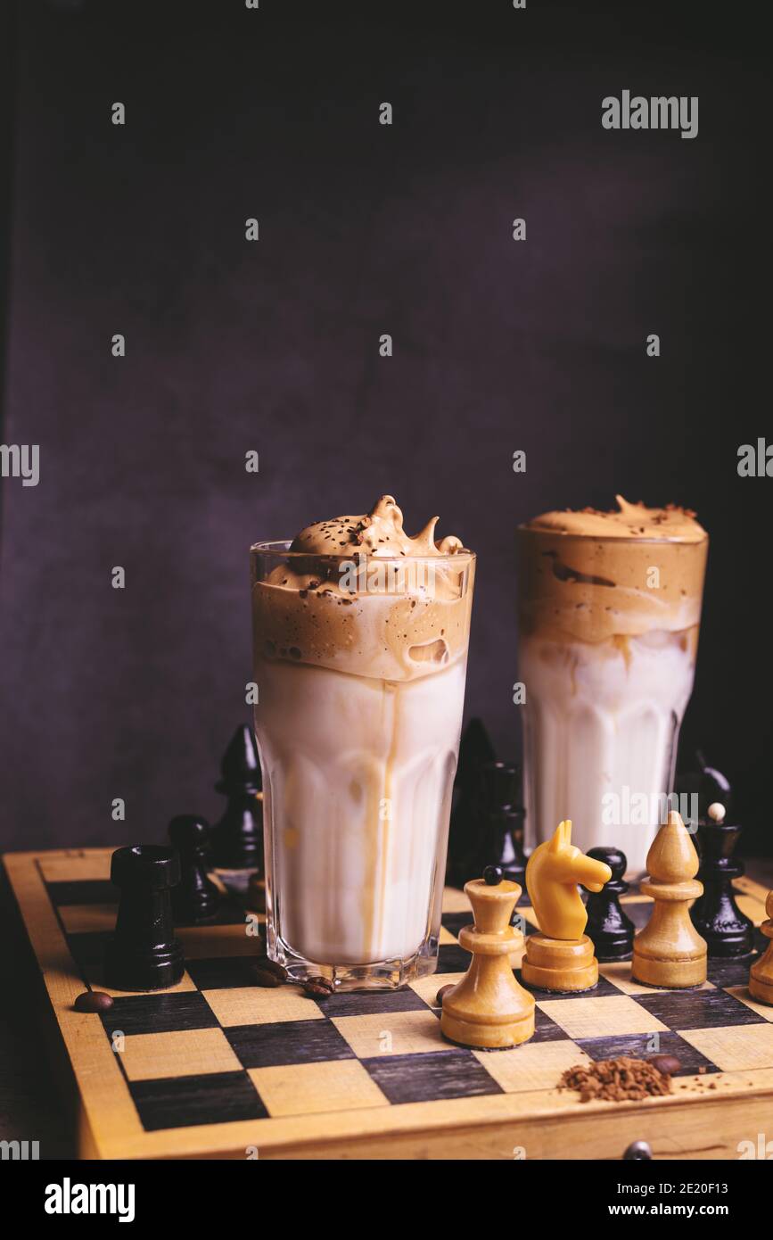 Dalgona Kaffee. Schlagsahngetränk mit Instant-Kaffee beliebt in Korea cremigen Cocktail in hohen Gläsern mit Schach auf Holzchessboard dekoriert Stockfoto