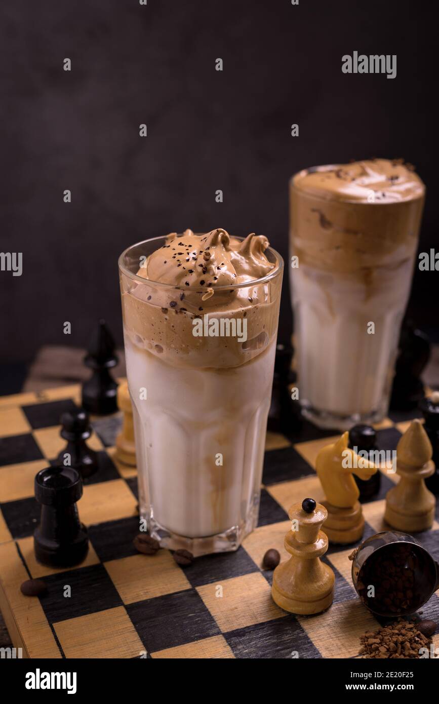 Dalgona Kaffee. Schlagsahngetränk mit Instant-Kaffee beliebt in Korea cremigen Cocktail in hohen Gläsern mit Schach auf Holzchessboard dekoriert Stockfoto