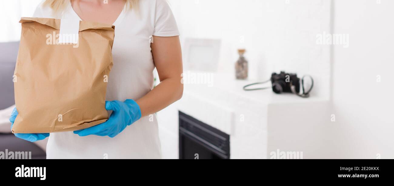 Junge Frau trägt medizinische Maske Empfangen Paket von der Lieferung in Innenräumen. Verhinderung der Verbreitung von Viren Stockfoto