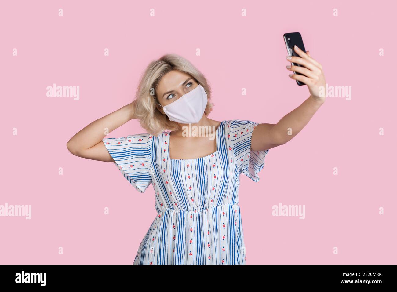 Charmante Dame macht ein Selfie auf einer rosa Wand Beim Tragen einer Maske und Sommerkleid Stockfoto